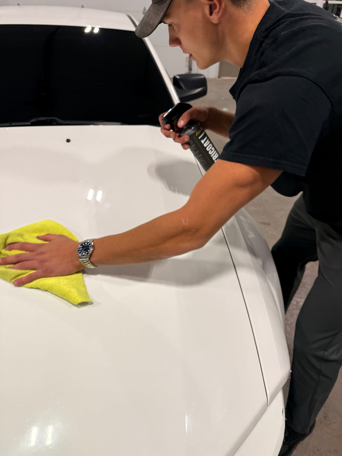 Golden Mobile Detailing technician buffing GoldenX Tricoat spray wax into a white car hood with a yellow microfiber towel